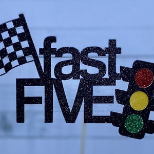 May include: Black glitter cake topper with the words "fast five" and a checkered flag and a traffic light with red, yellow, and green lights.