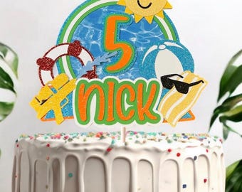 May include: A cake topper with a summer theme, featuring a smiling sun wearing sunglasses, a beach ball, and a life preserver. The number 5 is in orange, and the name "NICK" is in green and orange. The cake is white with colorful sprinkles.