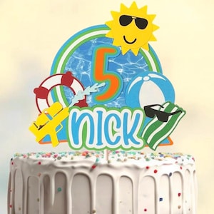 May include: A cake topper with a summer theme, featuring a yellow sun wearing sunglasses, a blue and orange number 5, and the name "Nick". Other elements include a beach ball, a life preserver, and a water gun.