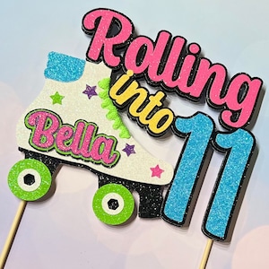 May include: A white roller skate with green wheels and pink glitter. The skate has the name "Bella" on it and the words "Rolling into 11" in pink and yellow glitter.