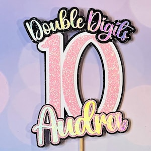 May include: Pink and black glitter cake topper with the number 10 and the words "Double Digits" and "Audra".