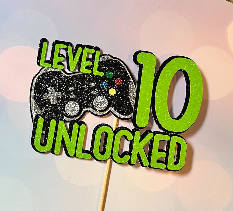 K&ouml;nnte beinhalten: Gr&uuml;ner und schwarzer Tortendekor mit dem Text "Level 10 Unlocked" und einem schwarzen und silbernen Videospiel-Controller.