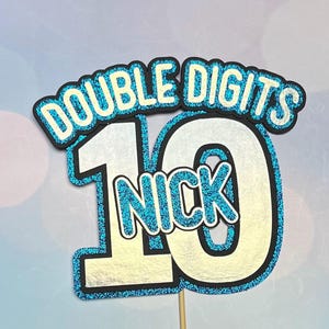 May include: Blue and silver glitter cake topper with the text "Double Digits" and the number "10" with the name "Nick" in the center.