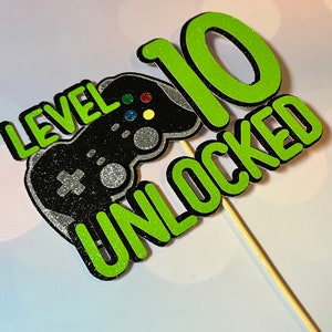 K&ouml;nnte beinhalten: Gr&uuml;ner und schwarzer Tortendekor mit einem Videospiel-Controller und dem Text "Level 10 freigeschaltet".