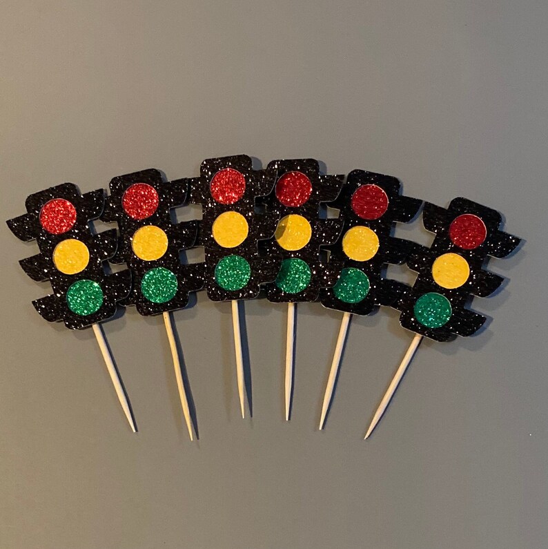 Op de afbeelding: Zes zwarte en glitterende verkeerslicht cupcake toppers met rode, gele en groene lampjes. De toppers zijn bevestigd aan houten stokjes.