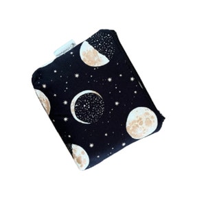 Może przedstawiać: Czarna kosmetyczka zapinana na zamek błyskawiczny z wzorem księżyca i gwiazd. Kosmetyczka jest wykonana z tkaniny i ma biały zamek błyskawiczny.