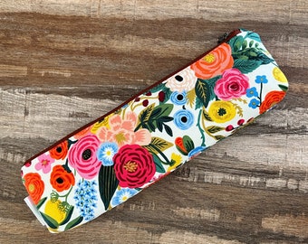 May include: A white fabric pencil case with a floral pattern. The pattern features red, pink, yellow, blue, and green flowers on a white background. The case has a brown zipper.