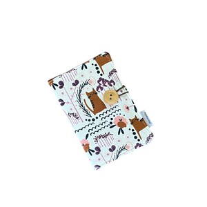 以下が含まれることがあります： 猫と花の模様が入った水色の布製ケース。木製のボタン留めと茶色の革ループが付いています。模様には茶色の猫、ピンクの花、紫の葉が含まれています。