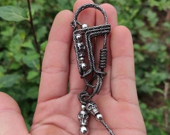 May include: A silver skull keychain with a twisted wire design and a small skull charm. The keychain is held in a hand.