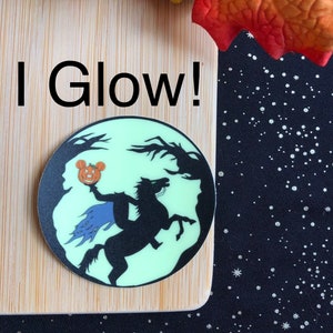 May include: A glow-in-the-dark sticker featuring a silhouette of the Headless Horseman riding a horse, holding a jack-o'-lantern with Mickey Mouse's face on it. The sticker is on a wooden surface with the text "I Glow!" written below it.