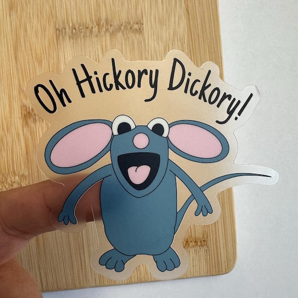 May include: A clear sticker with a cartoon mouse with pink ears and a blue body. The mouse is smiling and has a pink tongue sticking out. The sticker says "Oh Hickory Dickory!" in black text.