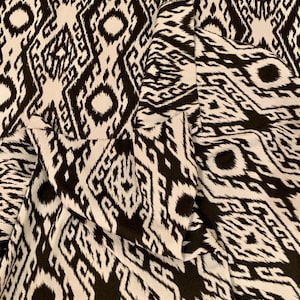 May include: Black and white fabric with an intricate geometric pattern. The fabric has a woven texture and a slightly shiny finish.