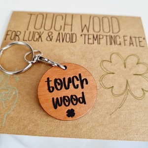May include: A wooden keychain with a round tag that says "touch wood" in black lettering. The keychain is attached to a silver key ring. The tag also has a small four-leaf clover carved into it.