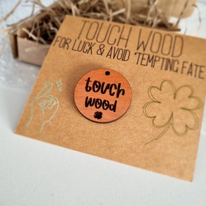 May include: A brown wooden circle with the text "touch wood" and a small four-leaf clover. The circle is on a brown card with the text "Touch Wood for Luck & Avoid Tempting Fate".