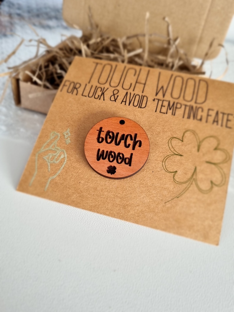 May include: A brown wooden circle with the text "touch wood" and a small four-leaf clover. The circle is on a brown card with the text "Touch Wood for Luck & Avoid Tempting Fate".