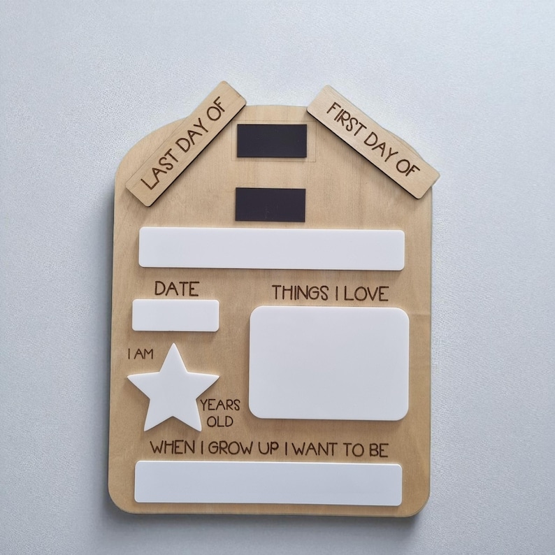 May include: Wooden school memory board with white and black details. The board features spaces for "Last Day Of" and "First Day Of" labels, a date, "Things I Love", and "When I Grow Up I Want To Be". A star shape is also included.