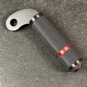 May include: A black metal handle with a textured knurled grip, a curved mounting bracket featuring a circular hole, and a thin red accent ring. The end cap of the handle displays the word HYBRID in red lettering, providing a clear view of the component's design and construction details.