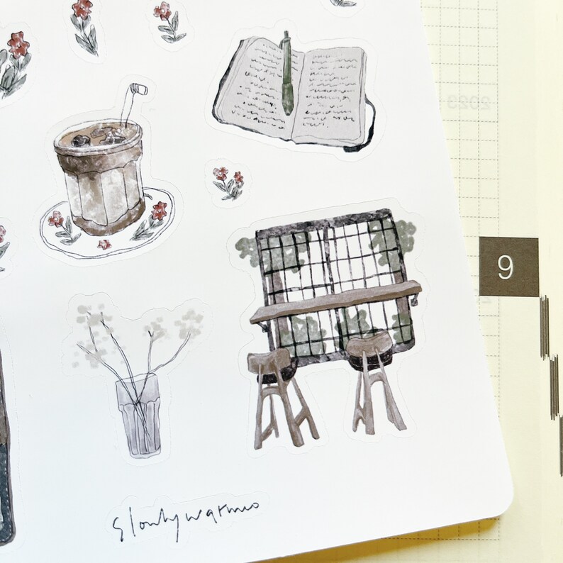 May include: A set of watercolor stickers featuring a coffee cup, a book, a window with a table and chairs, and flowers. The stickers are on a white background and have a hand-drawn style. The text "Slowly warming" is written at the bottom of the image.