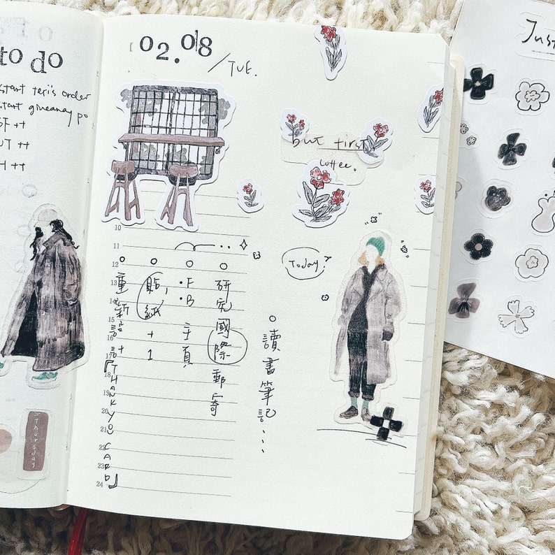 May include: A page from a planner with the date 02.08 written at the top. The page is divided into sections with handwritten notes and drawings. The notes include the words "to do", "but first coffee", and "Today". There are also several stickers on the page, including a small cafe scene, a person in a coat, and a few flowers.