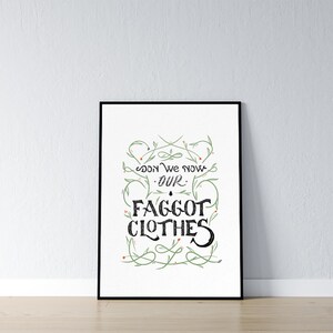 May include: A framed art print with the words "Soon We Now Our Faggot Clothes" in a decorative font. The text is black on a white background, with green floral accents. The frame is black.