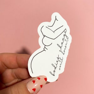 May include: A white sticker with a line drawing of a pregnant person. The text "bodies change, worth doesn't" is written on the sticker.