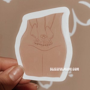 May include: A sticker with a line drawing of a person's lower body with a scar and flowers growing from it. The text "blissfulmami.com" is at the bottom of the sticker.