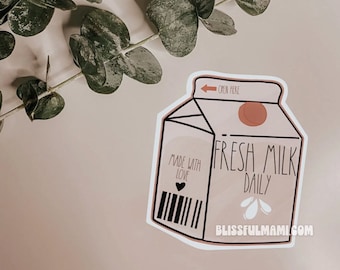 May include: A sticker of a milk carton with the text "Fresh Milk Daily" and "Made with Love" with a heart. The carton is beige with a brown top and a black outline. The sticker has a white background and the text "Blissfulmami.com" at the bottom.