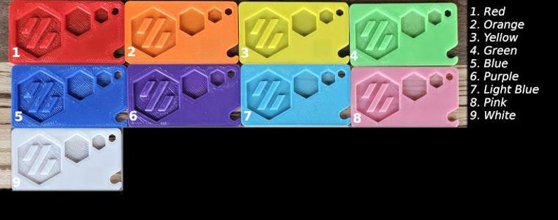 May include: Nine plastic keyrings in different colours, including red, orange, yellow, green, blue, purple, light blue, pink, and white. Each keyring features a hexagonal design with the letters "HG" inside.