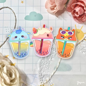 May include: Three cartoon animal bubble tea stickers. The first sticker is a blue and yellow bubble tea with a goat face. The second sticker is a pink and white bubble tea with a unicorn face. The third sticker is an orange and yellow bubble tea with a fox face.