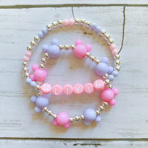 May include: A pink and purple beaded bracelet with silver beads and a name charm that says "OLIVIA".
