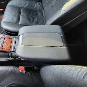 Puede incluir: Vista interior de un coche con asientos de cuero negro y molduras de madera. La imagen muestra los asientos delanteros, la consola central y el salpicadero. Se ve la palanca de cambios, junto con el reposabrazos y los cinturones de seguridad.