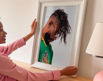 May include: A framed portrait of a person with dreadlocks wearing a green and yellow shirt and glasses. The person is looking down at the ground.