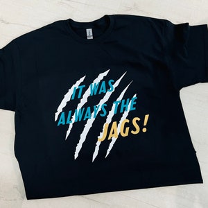 May include: Black t-shirt with a white claw mark design and the text "It was always the JAGS!" in teal and yellow.