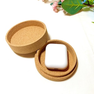 Könnte beinhalten: Eine runde Korkbox mit Deckel, geöffnet, um ein weißes, rechteckiges Etui im Inneren zu zeigen.