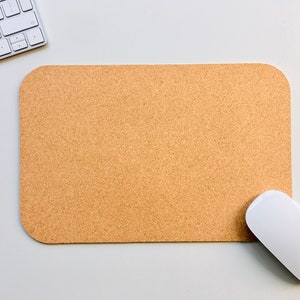 Op de afbeelding: Een witte computermuis ligt op een kurken bureauonderlegger. De onderlegger is rechthoekig en heeft een lichtbruine kleur.