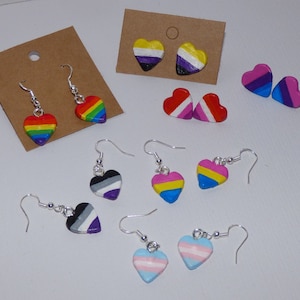 May include: A selection of heart-shaped earrings featuring different pride flag designs, such as rainbow, transgender, bisexual, pansexual, and asexual flags.