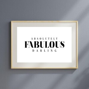 May include: A framed print with the words "ABSOLUTELY FABULOUS DARLING" in black text on a white background. The frame is a light wood color, and the background is a solid gray.