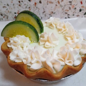 May include: A key lime pie with a light green filling and a flaky crust. The pie is topped with white whipped cream and garnished with two slices of lime.