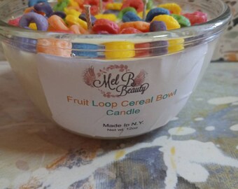 May include: A clear glass bowl filled with a white candle and colorful cereal-shaped decorations. The label reads "Mel B Beauty Fruit Loop Cereal Bowl Candle Made in N.Y. Net wt 12oz."