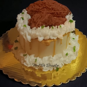 May include: A white cake with gold drizzled icing and a chocolate-brown frosting topping. The cake is decorated with green sprinkles and the words "Mel Be Beauty" are written on the side.