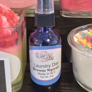 May include: A blue glass bottle with a black spray top and a white label that reads "Mel B Beauty Laundry Day Room Spray Made In N.Y. Net Wt. 2 oz".