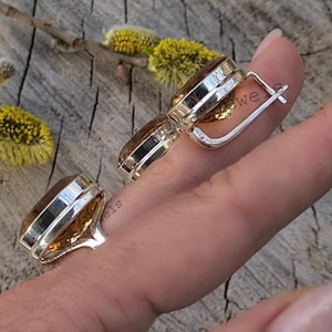 Puede incluir: Un par de pendientes de plata con una piedra preciosa redonda de color naranja. Los pendientes est&aacute;n en una mano, y la mano sostiene un anillo con una piedra preciosa similar.
