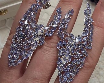 May include: A pair of elegant earrings featuring a cluster of light purple gemstones. The earrings have a unique, asymmetrical design, with the text "Vamika Jewels" visible. The gemstones are set in a silver-toned metal, creating a sparkling effect.