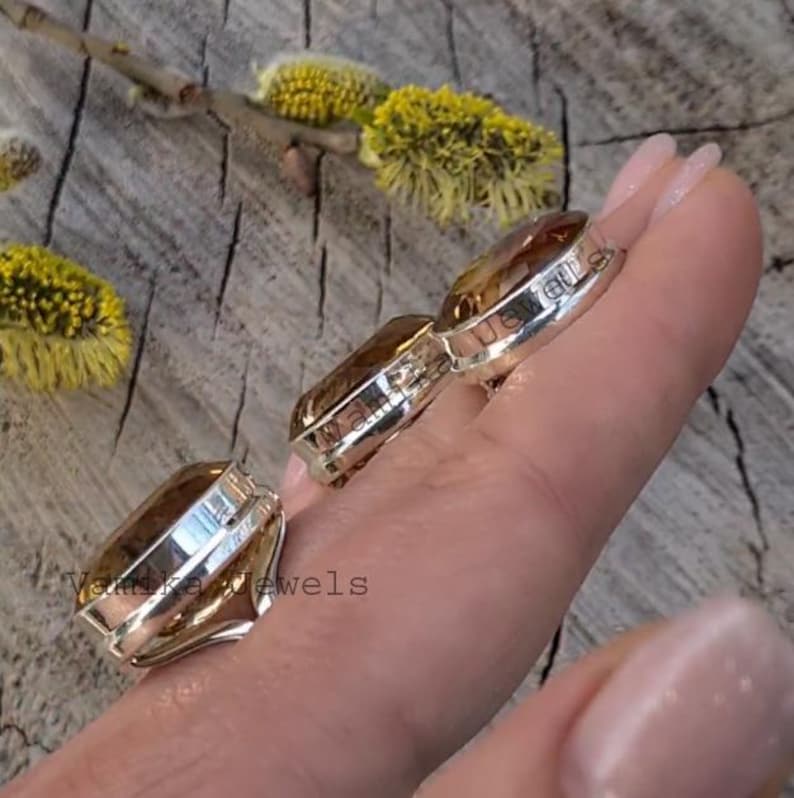 Puede incluir: Tres anillos de plata con grandes piedras ovaladas de color marr&oacute;n. Los anillos est&aacute;n apilados en una mano, con el anillo m&aacute;s grande en la parte inferior y el anillo m&aacute;s peque&ntilde;o en la parte superior.