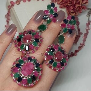 May include: A three-piece jewelry set featuring a ring and a pair of earrings. The ring and earrings have a floral design with a large pink center stone surrounded by smaller green, blue, and pink stones. The earrings are dangling.