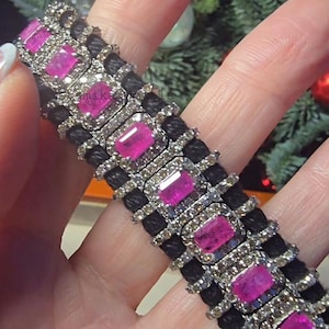 May include: A close-up of a bracelet featuring rectangular pink gemstones set in a silver frame, alternating with black woven bands. The bracelet is adorned with small, clear gemstones around the pink stones.