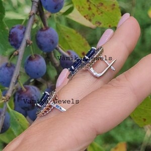May include: A pair of silver earrings featuring blue gemstones and black accents. The earrings are circular in shape with a small hook.