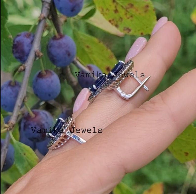 May include: A pair of silver earrings featuring blue gemstones and black accents. The earrings are circular in shape with a small hook.