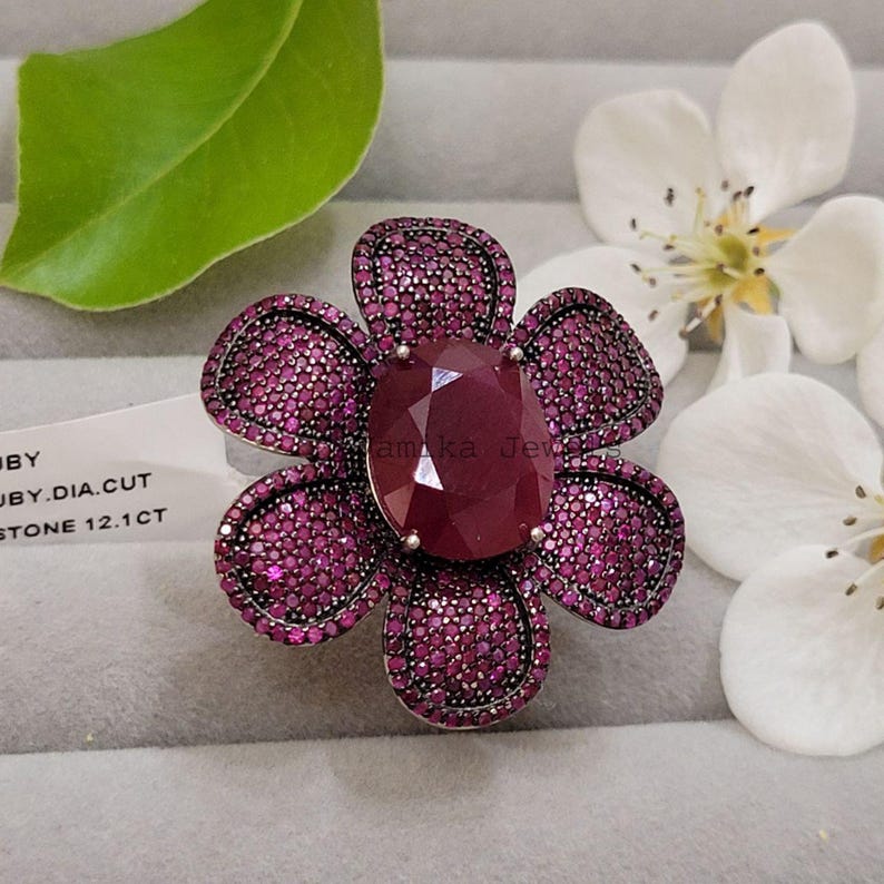Pu&ograve; includere: Anello a forma di fiore con una grande pietra centrale di rubino sfaccettato. I petali sono incastonati con pietre preziose rosa scuro pi&ugrave; piccole. L'anello &egrave; montato su una fascia d'argento. Un gioiello di grande effetto.