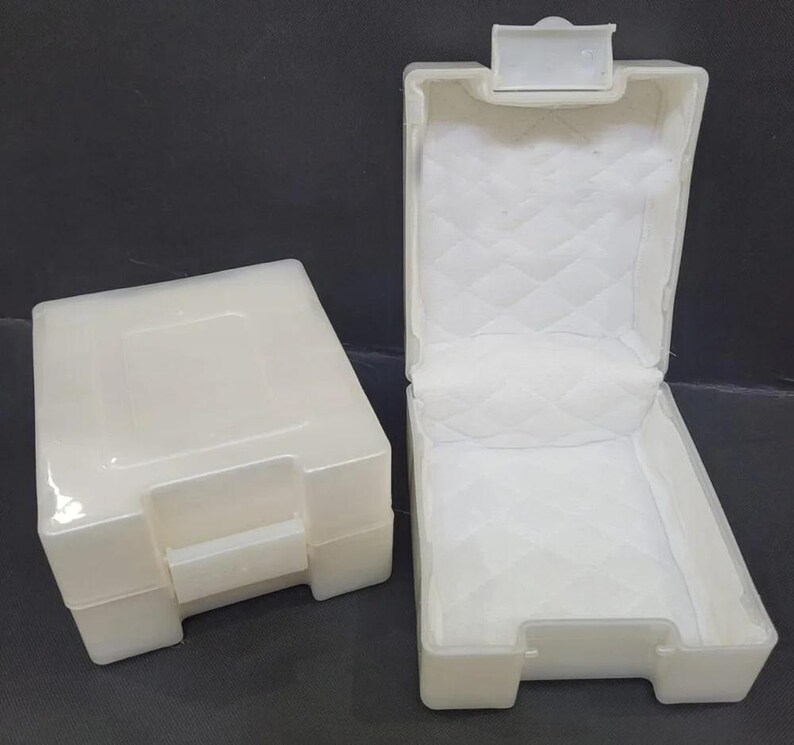 Pu&ograve; includere: Due scatole di plastica bianco sporco, una chiusa e una aperta. La scatola aperta ha un interno bianco trapuntato. Entrambe le scatole hanno una forma rettangolare con chiusura a scatto. Le scatole sono probabilmente per la conservazione o l'esposizione di piccoli oggetti.